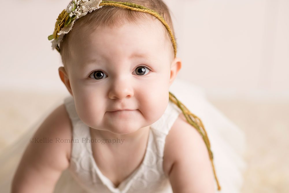 pastel milestone session one year old girl having pics taken in Milwaukee Wisconsin studio she's from Illinois the photo is a close up of her face smirking at the camera she's wearing a white dress and a headband