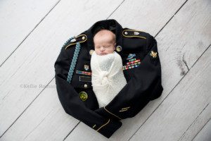texas roots a newborn boy from kenosha in Milwaukee photographers studio he's wrapped in a white cloth swaddle and is laying onto of his fathers army uniform the swaddle has a decorative knot in the center