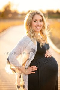 a cold night on the beach for maternity photo shoot a women standing on a wood walkway who is pregnant from Illinois is being photographed by a Milwaukee photographer she is standing with sunshine behind her and going through her blonde hair she is holding onto her pregnant belly