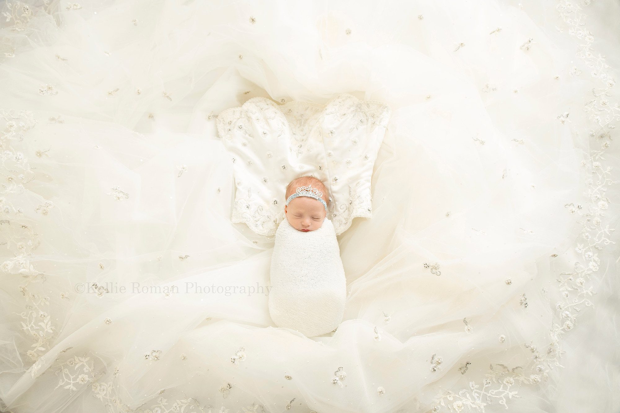 sweet little sister a newborn photo session in Milwaukee photography studio with a newborn little girl from Racine. She is in an ivory swaddle and is laid onto of her mothers wedding beaded wedding gown. Newborn is sleeping with a crown headband on