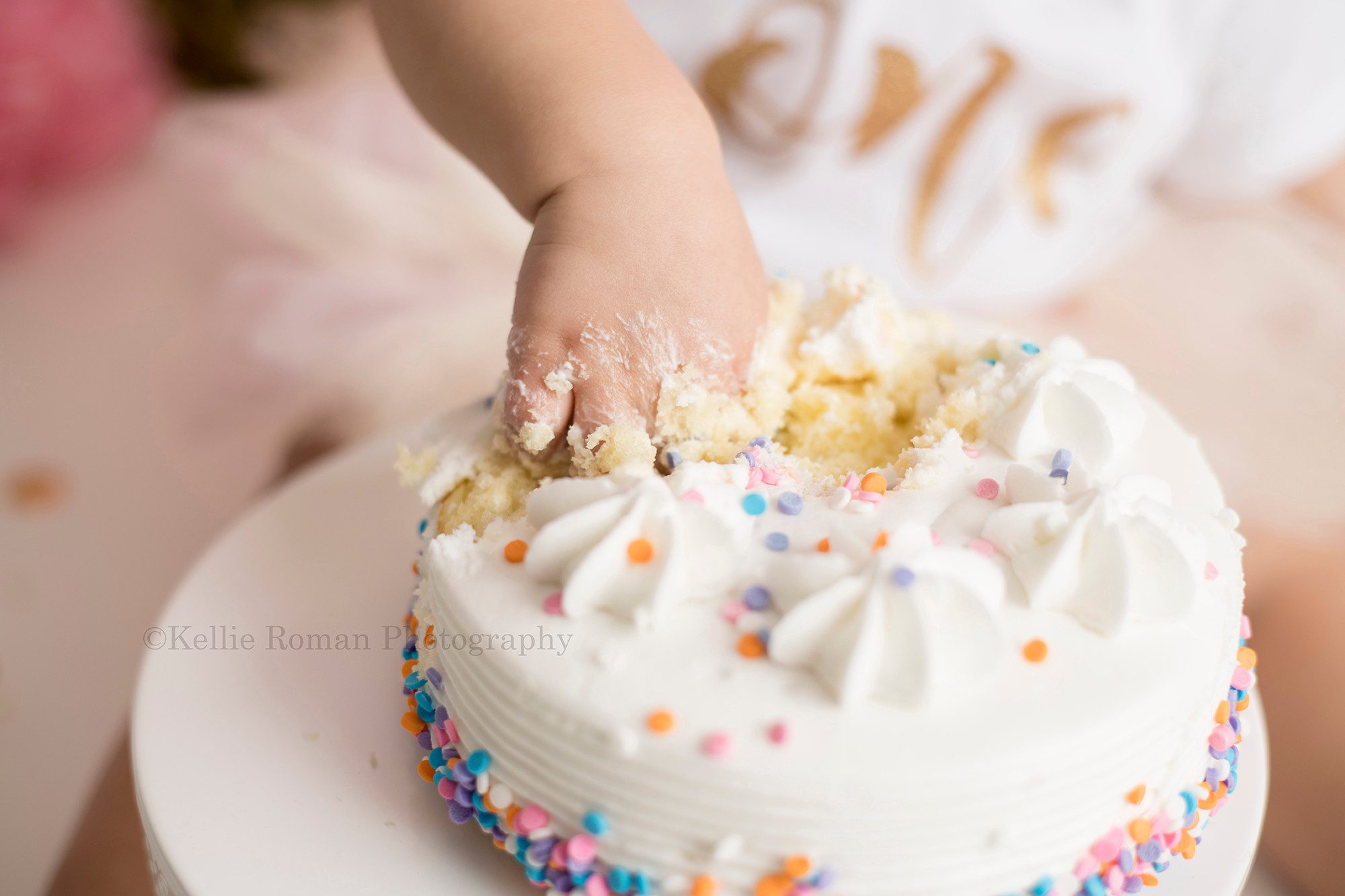 dig in a close up shot of a one year old girl from waukesha in a Milwaukee photographer studio. she's smashing her hand into a white cake with colored sprinkles