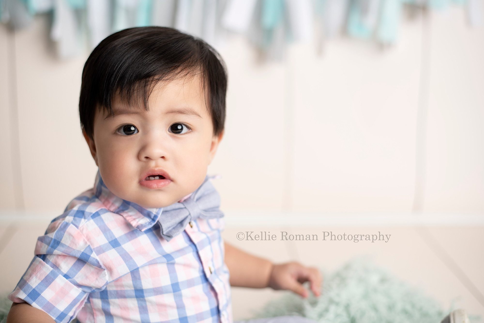 up up and away a one year old boy from kenosha at his milestone session in Milwaukee studio looking serious at the camera. close up of his face. He's wearing a plaid shirt and sitting on a green furry rug