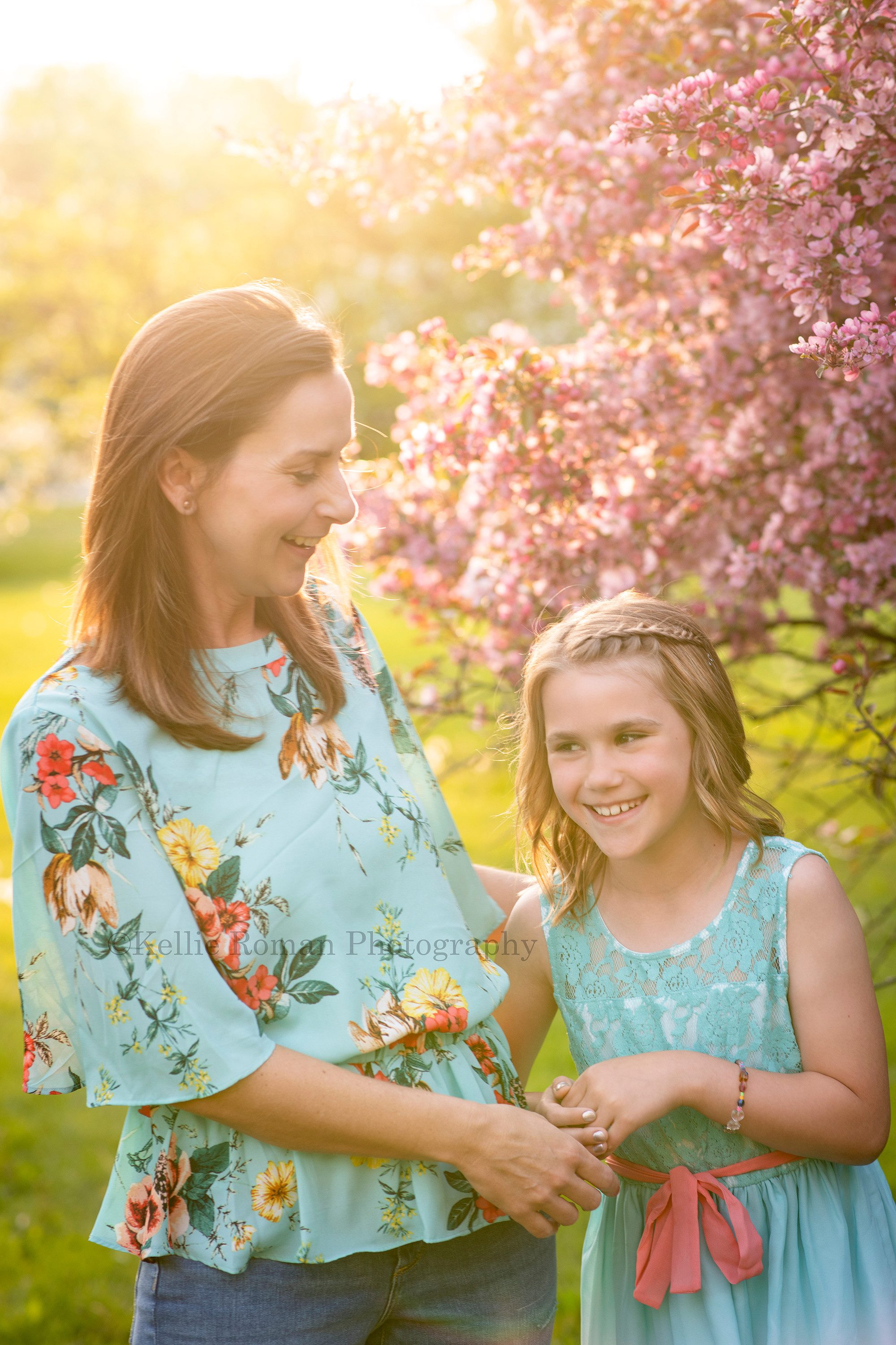 sunlit blossoms a mother and daughter from kenosha standing in a Milwaukee parking playing around they are smiling and laughing and interacting with each other the sunshine is peaking behind them through blossoms on trees