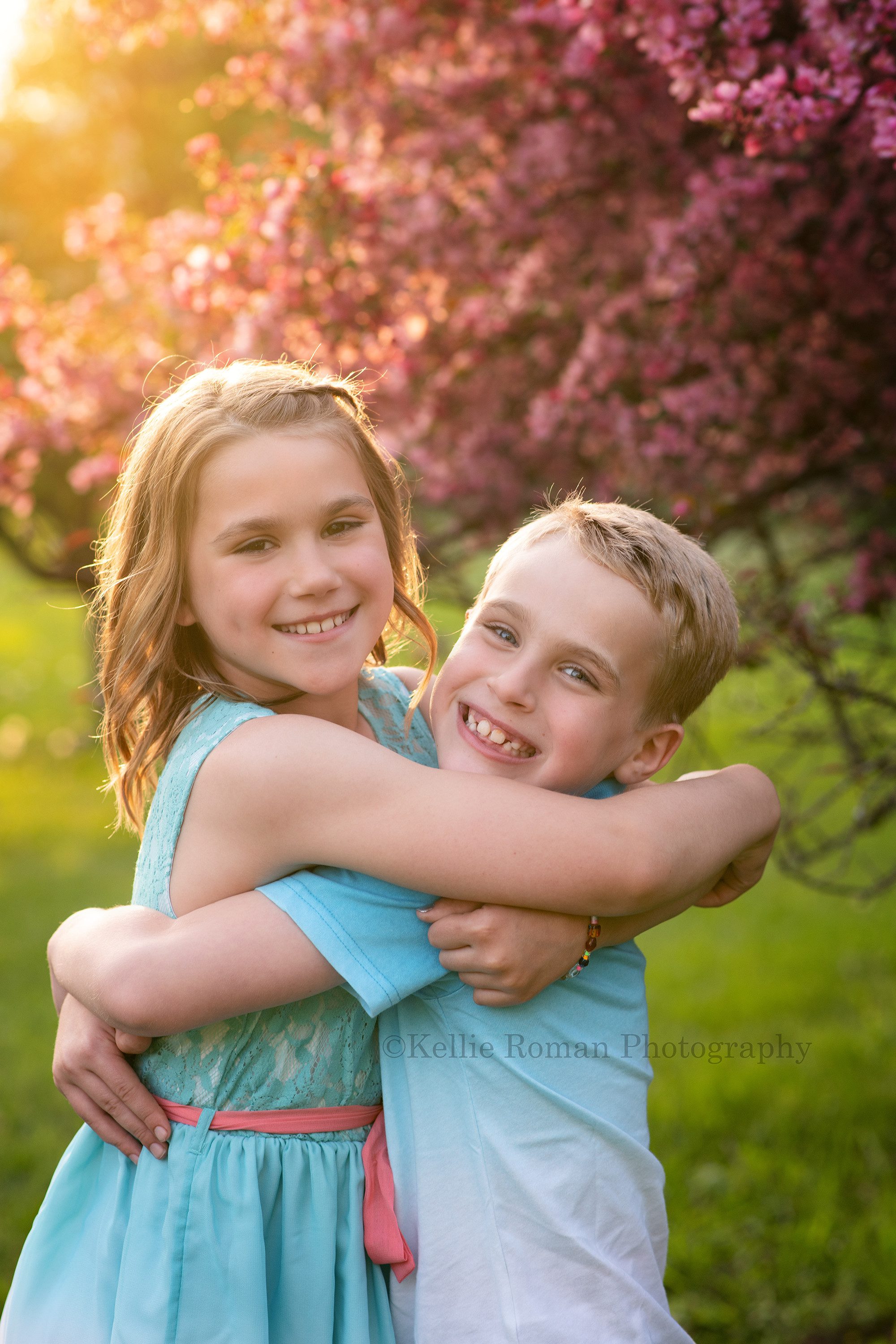 sunlit blossoms a brother and sister hugging in a Milwaukee park infant of pink blooming trees the sunlight is peaking through the trees behind them