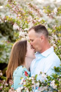 sunlit blossoms a married couple standing in a Milwaukee park surrounded by flowering trees. husband is kissing his wife on the forehead