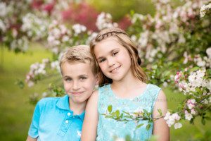 a brother and sister standing behind a stem of flowering trees smiling at the camera they are both wearing blue and are in Milwaukee
