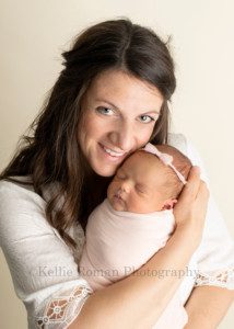 perfect newborn girl a little newborn baby girl who's wrapped in a soft pink swaddle fabric is being held tight by her mother who is from kenosha Wisconsin her mom is wearing a white dress and is looking at the camera