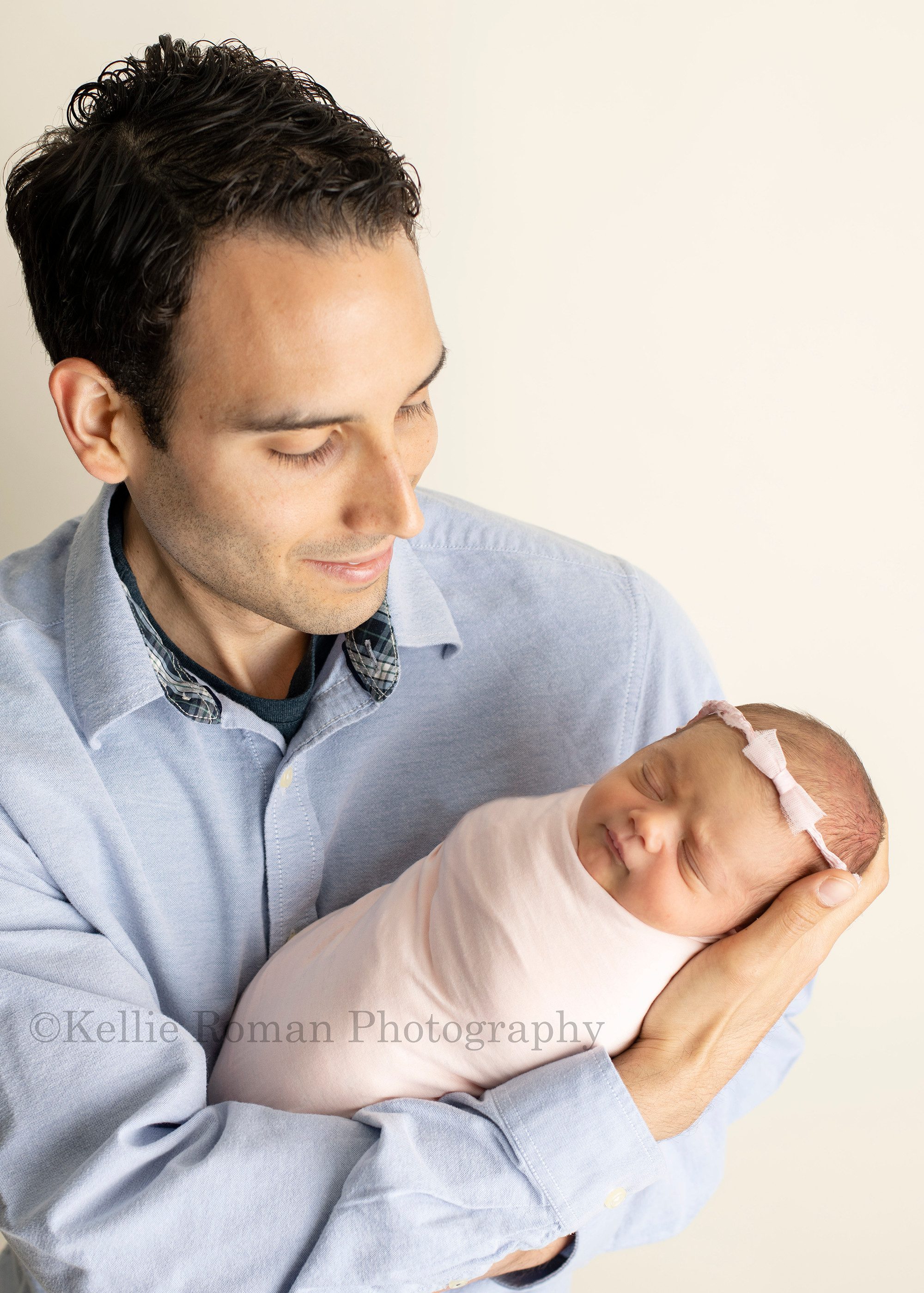 perfect newborn girl a little newborn baby wrapped in a pink swaddle being held by her dad in a milwaukee studio her dad is wearing a blue button up shirt