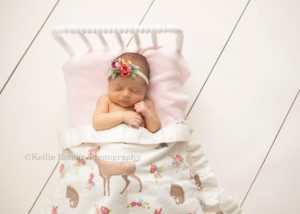 perfect newborn girl a newborn little girl is posed in milwaukee photographers studio sleeping on top of a white bed she has her hand up by her face and is covered by a blanket her mom and dad brought in it was woodland creatures on it