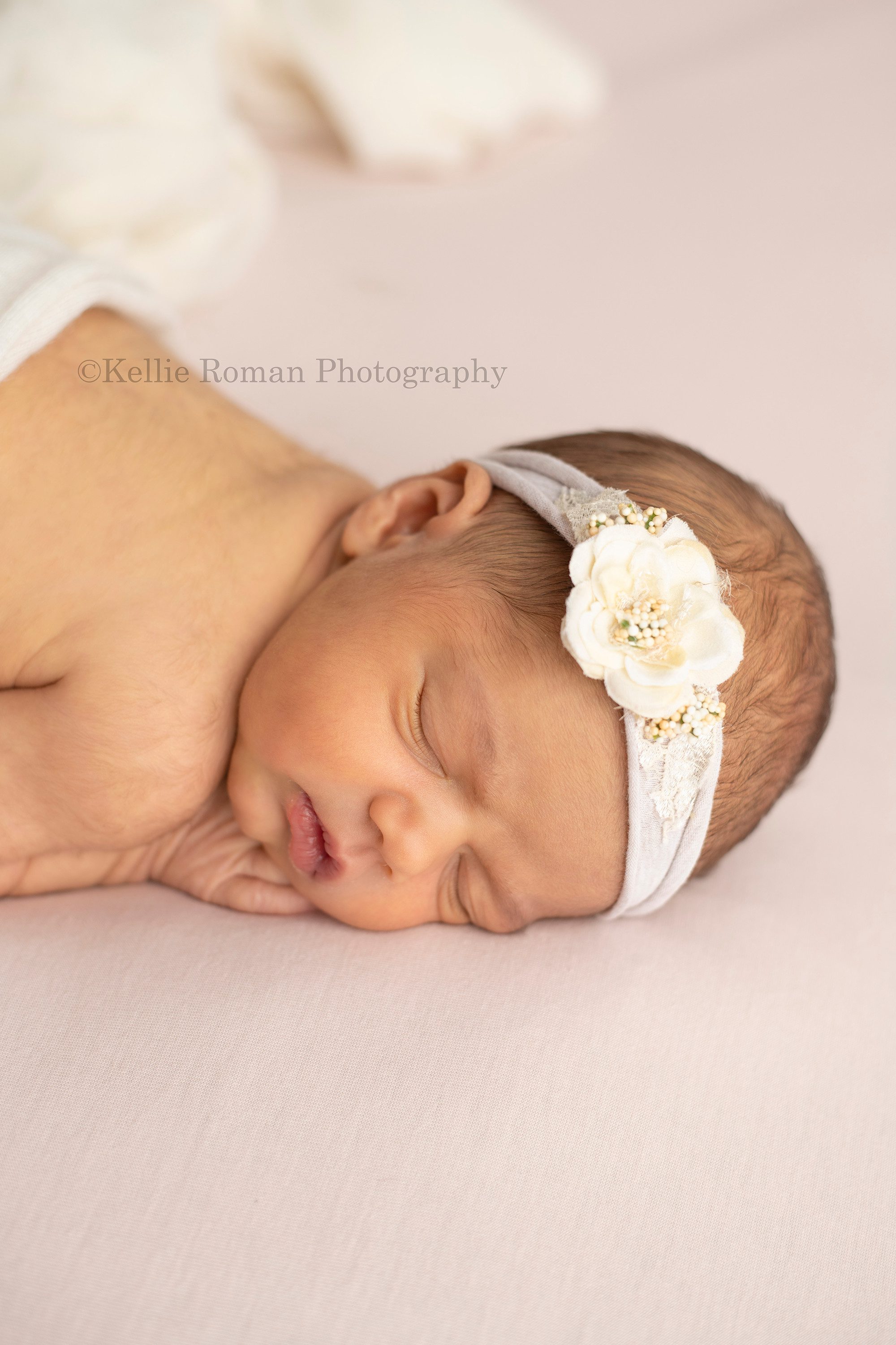 perfect newborn girl baby girl in milwaukee photographers studio she's from Madison Wisconsin and her parents are from kenosha Wisconsin she's sleeping posed with her hands under her cheeks onto of a very light pink blanket she has a white floral headband on