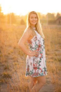 senior beach session a high school senior from kenosha on a beach with golden sunlight behind her she has her hand on her hip and is looking backwards she is surrounded by beach grass and is being photographed by a milwaukee photographer