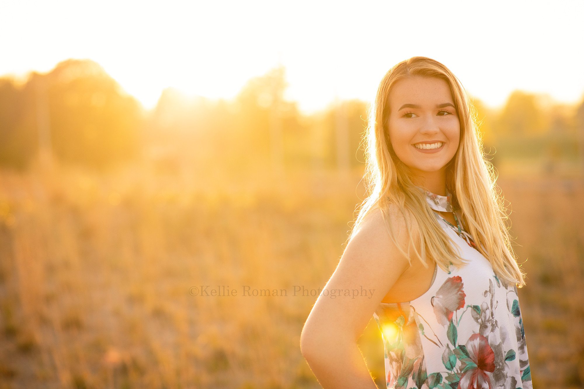 senior beach session a high school senior from kenosha is standing on the beach in kenosha with her hand on her hip she is looking backwards and the sun is glowing from behind her she's being photographed by a milwaukee senior photographer