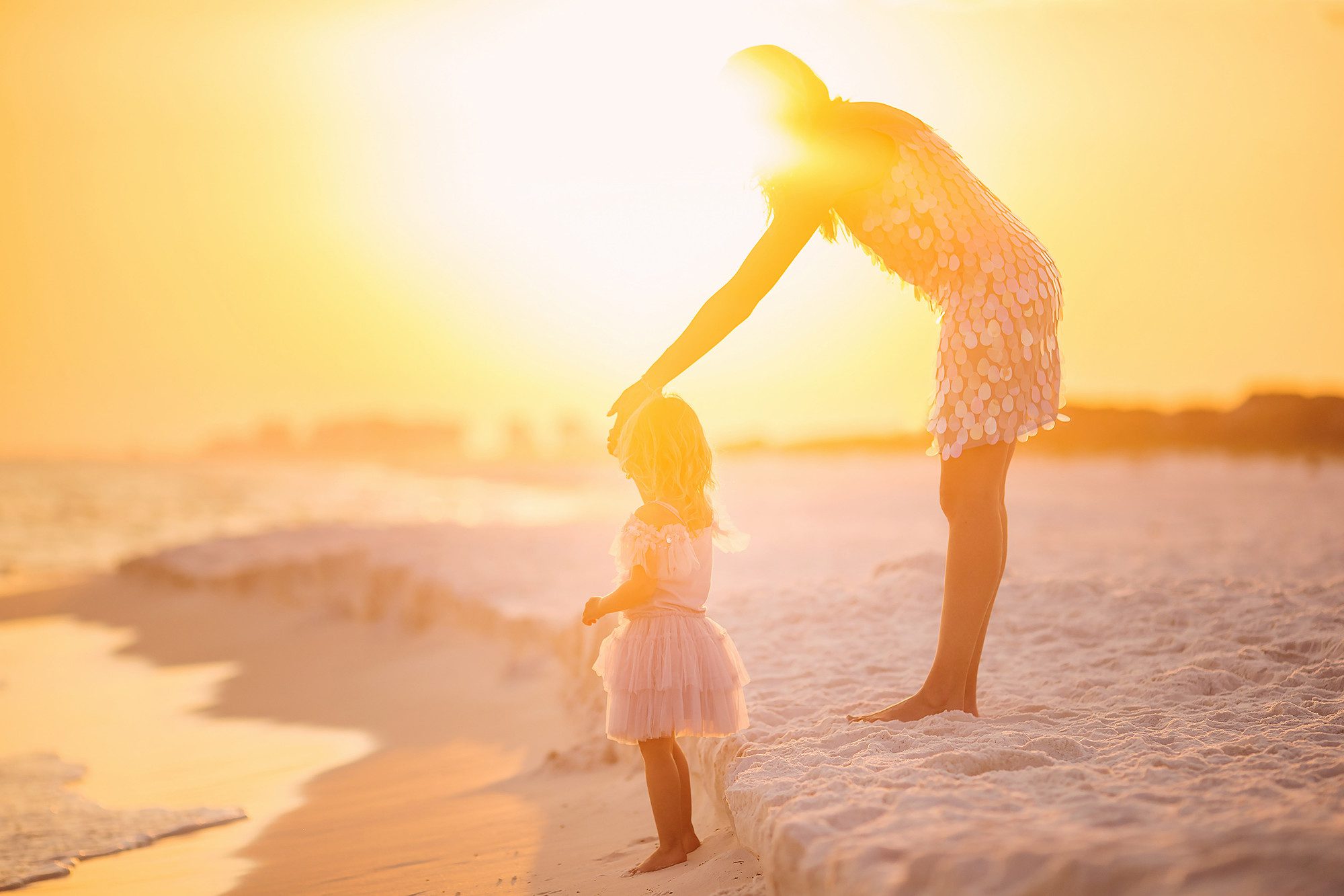photography session with kanas Pitts a mother and daughter on the beach in Florida they are from milwaukee Wisconsin the mother is holding on to the daughters hand they are wearing pastel colored dresses and the sun is setting behind them