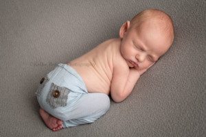 newborn twin pics one little newborn baby posed onto of a grey blanket in milwaukee photographers studio he's sleeping and is wearing light blue pants