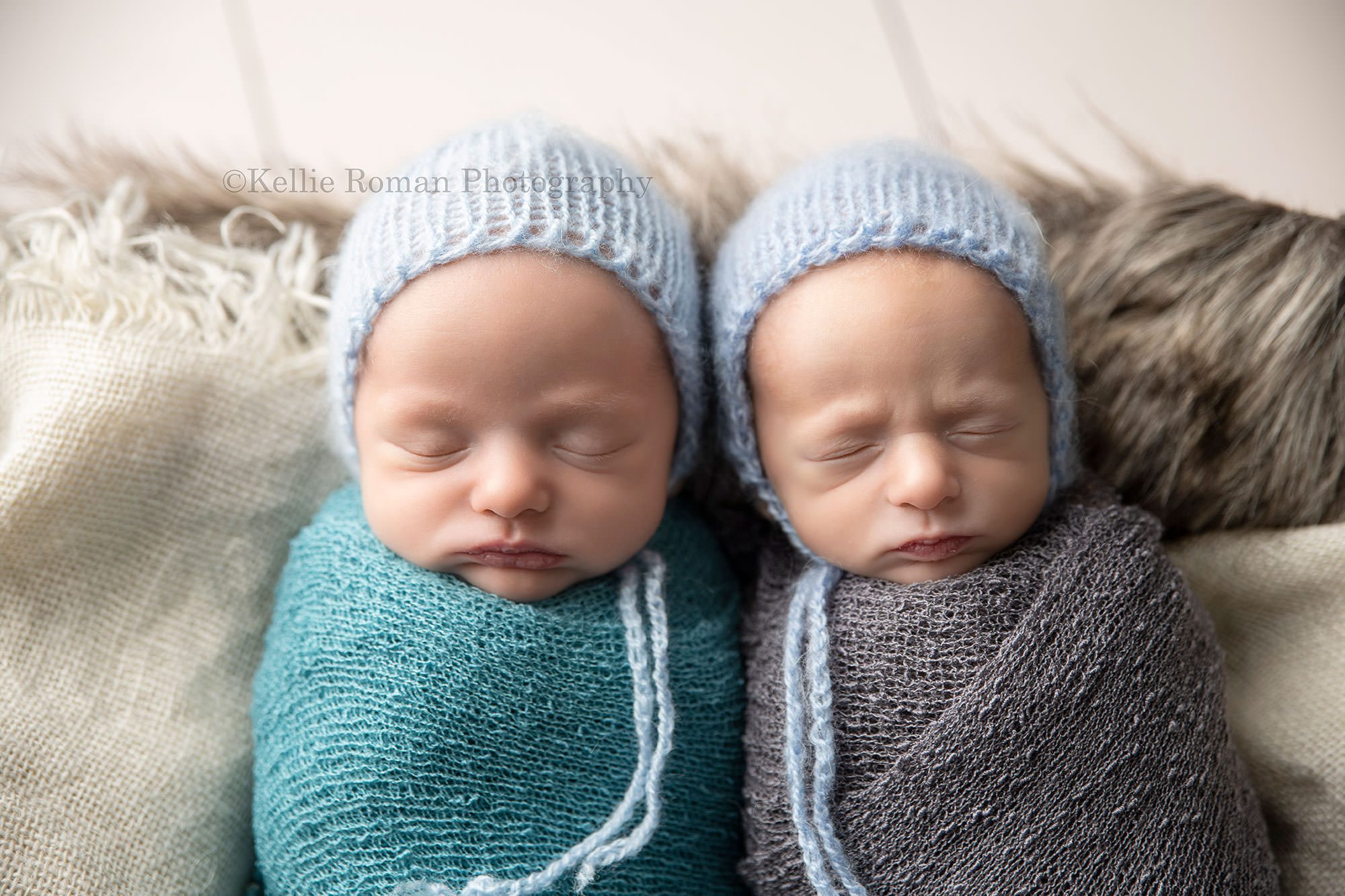 newborn twin pics two baby brothers are sleeping onto of burlap on their backs in a wood crate the babies are wrapped in grey and blue fabric and have blue bonnets on they are in a milwaukee photo studio