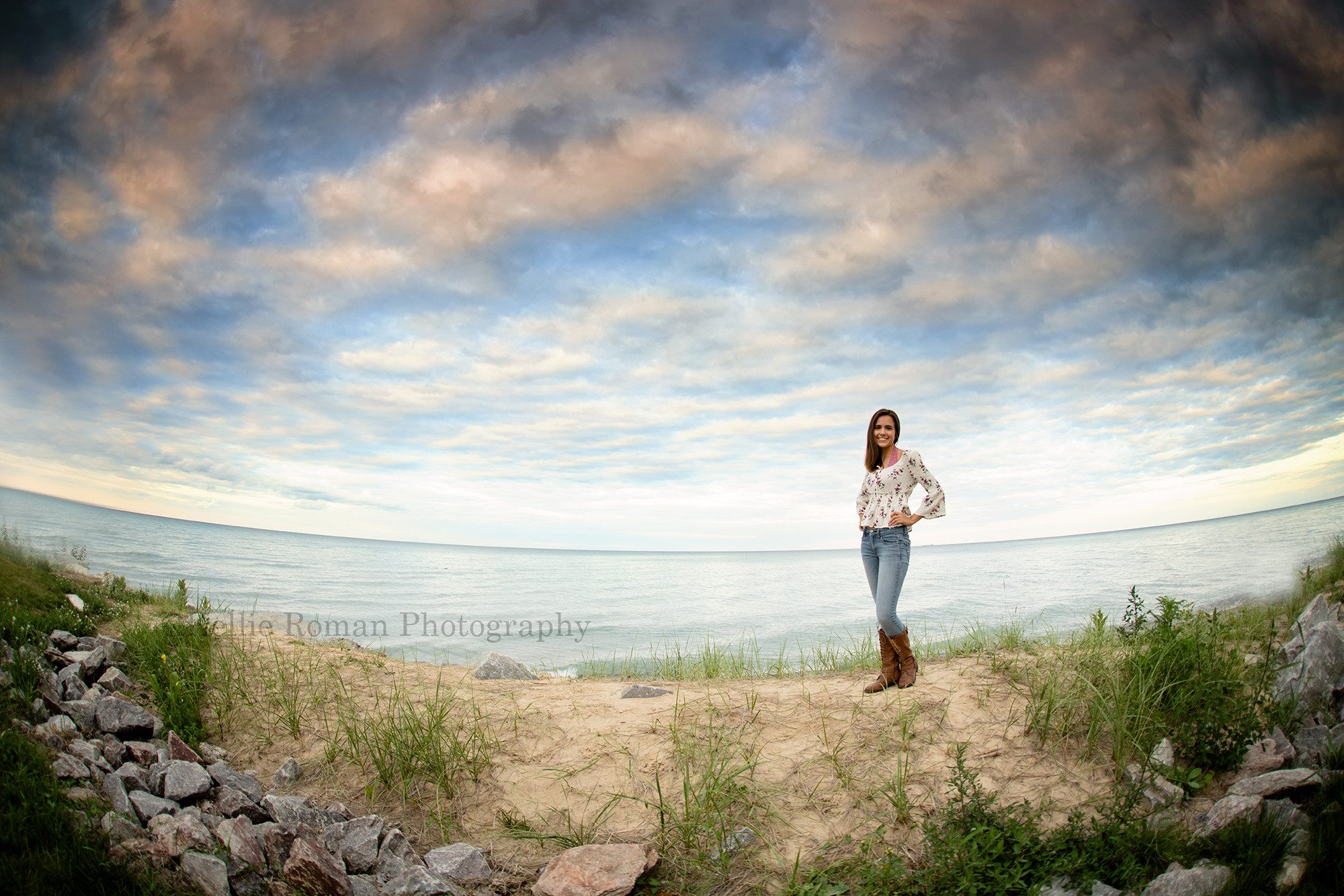 lighthouse senior pics a girl standing on a sand dune with Lake Michigan behind her the sky has very dramatic clouds with shades of colors