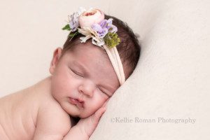 baby girl sleeping with her hands under her chin posed on top of a bean bag she is wearing a flower headband and is in a milwaukee photographer studio