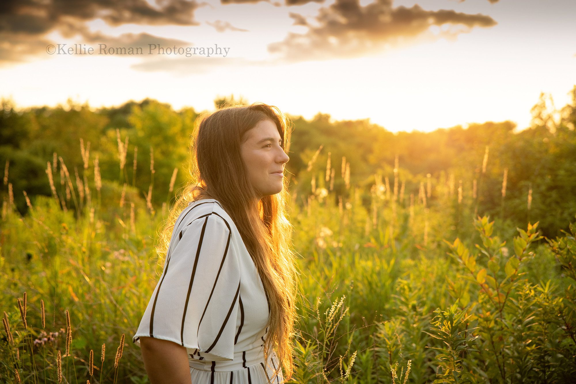 boho inspired a teenage girl standing in a field of tall green grass and flowers being lit up by the setting sun she has long hair and is looking off to the side