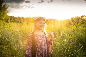 boho inspired a young girl with blond hair standing in a field of tall grass and flowers in Wisconsin she has on a boho outfit and is looking off to the side while the sun is setting behind her and making her hair glow