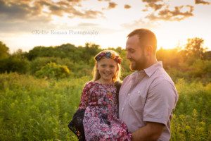 boho inspired session a father is twirling his daughter around in his arms in a field of tall grass the sun is setting behind them they are wearing shades of maroon and the father is looking at his daughter