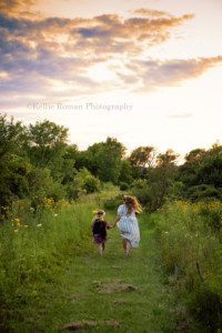 boho inspired session with two young girls in dressed running through a field the sunset is gorgeous and lighting up the clouds with shades of orange and purple