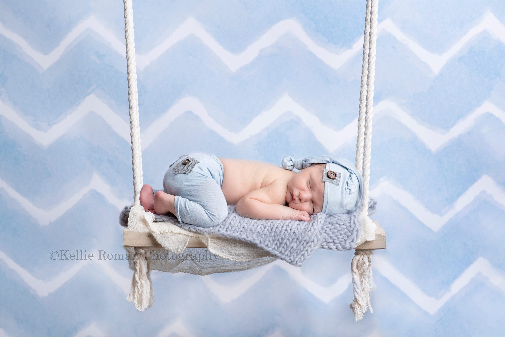 baby pics a newborn baby boy who is laying asleep on a wood swing he is in front of a blue and white chevron backdrop wearing light blue pants and a hat the image is a composite shot so it looks as if the swing is actually hanging with the newborn on it Milwaukee photographer is taking the image