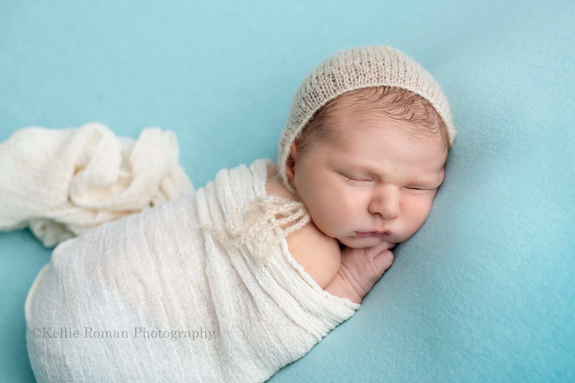 baby pics a newborn baby boy is laying asleep on a blue blanket he is posed with his hand under his chin and he is in a white swaddle wrap in a milwaukee photography studio