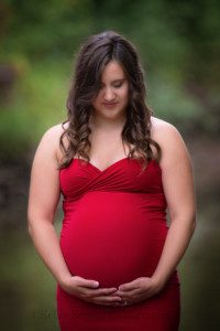 maternity gowns a close up shot of a women wearing a red tight maternity gown in kenosha Wisconsin she's looking down at her belly and has both hands on the bottom of her stomach