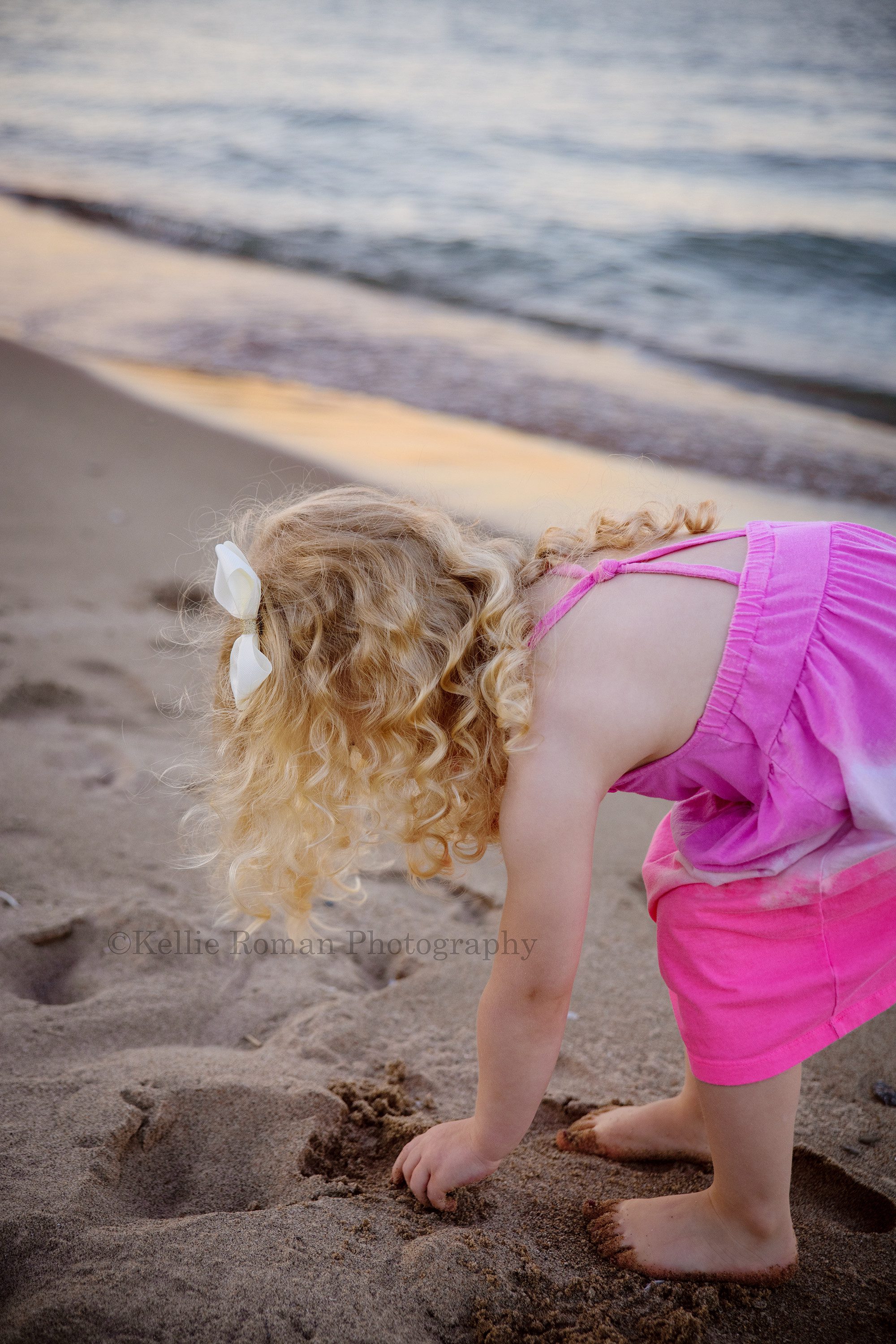 bubbles at the beach a young three year old girl wearing a bright pink dress is on the beach in milwaukee Wisconsin she is bending over and picking something up in the sand