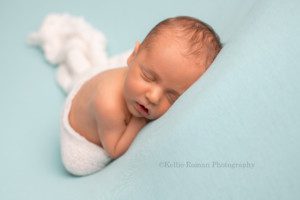 rainbow baby a newborn baby boy posed onto of light blue fabric with a cream swaddle over his butt and legs he is being photographed in milwaukee photography studio