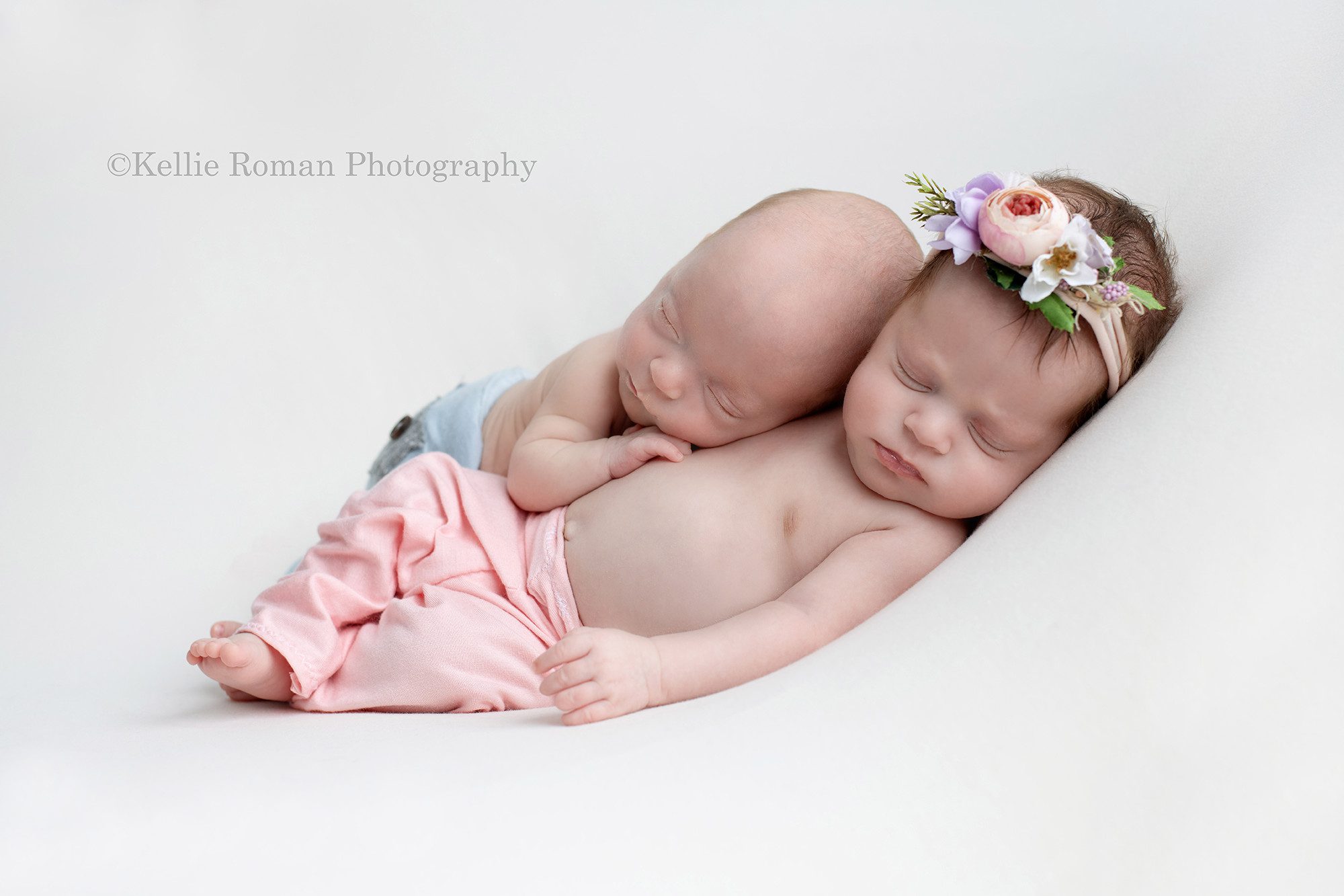 milwaukee twins a newborn brother and sister in milwaukee studio for photography the girl has on light pink pants with a floral pink headband and the boy is wearing light blue pants they are posed on top of a cream colored blanket on a beanbag the girl is on the bottom on her back and the boy is on his belly posed on top of the girls torso