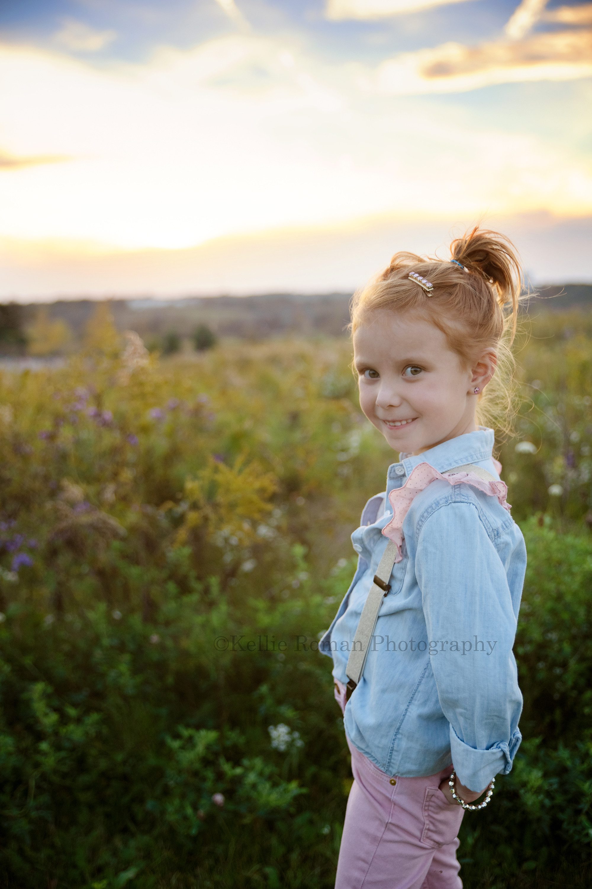 sunset milestone a young girl celebrating her sixth birthday is having photos taken in milwaukee Wisconsin park she is in a field of tall grass with a gorgeous sunset behind her she's wearing pink pants with a denim shirt and pink and gold suspenders