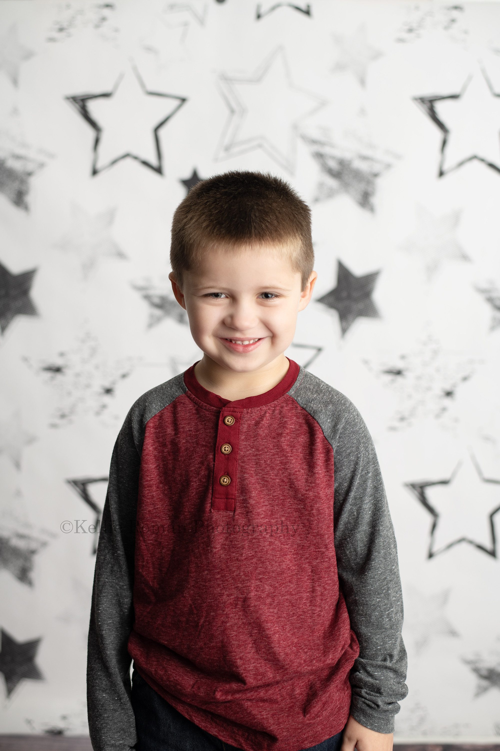 milwaukee milestone photographer a young boy celebrating his fourth birthday with photos is in milwaukee photographer studio he's in front of a white backdrop with black stars and is wearing a red and grey shirt