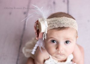 six month milestone a baby girl with a big headband on is in a greendale photography studio in milwaukee county the shot is from above and she is looking up with her big brown eyes and a very serious face