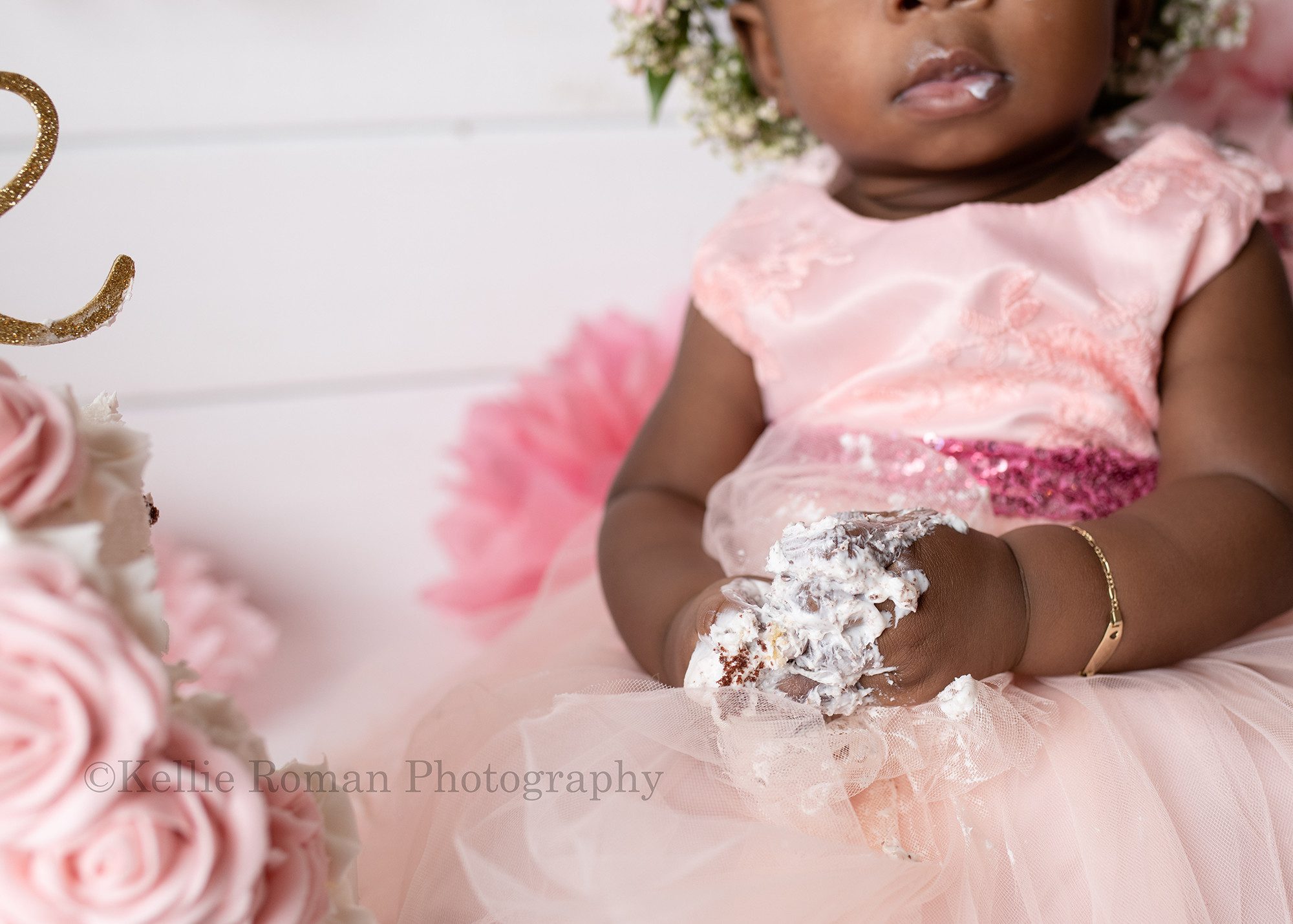 takes the cake a close up shot of a little one year old girls hands that are covered in white frosting she is in a milwaukee photographers studio for her cake smash session she's wearing a light pink dress and is sitting next to her two tier cake with light pink flowers