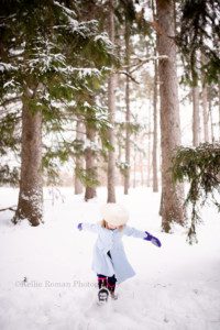 Milwaukee snowfall a little girl in a milwaukee county park is looking down and kicking at snow with her winter boots on she has a powder blue pea coat and a white fur hat she is surrounded by tall pine trees and snow