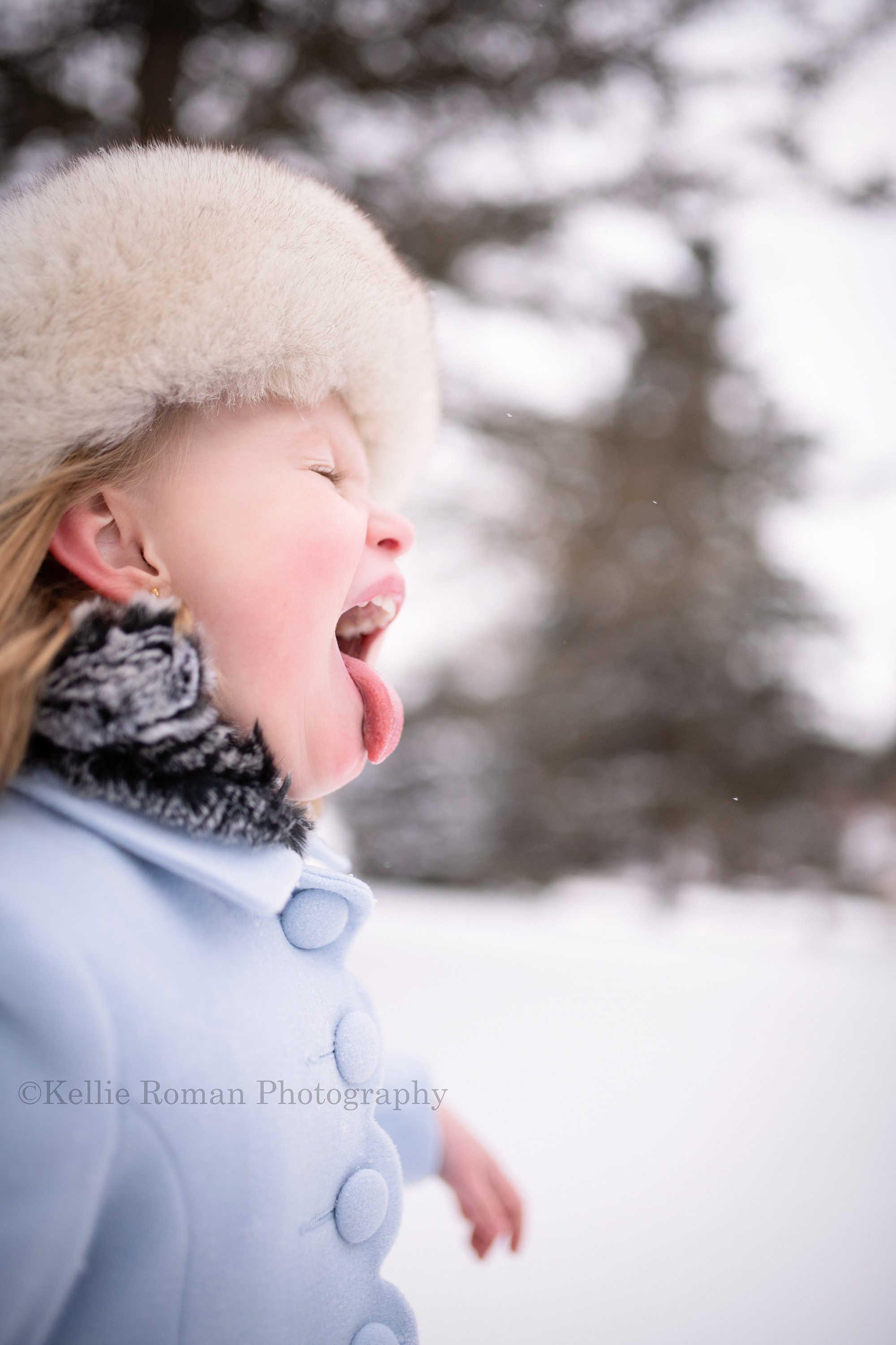 milwaukee snowfall a young 5 year old girl is outside in the snow in a Milwaukee County park. She has a powder blue pea coat on and a white fur hat. The image is a profile shot and she's sticking her tongue out with snow on it. She has her eyes closed.