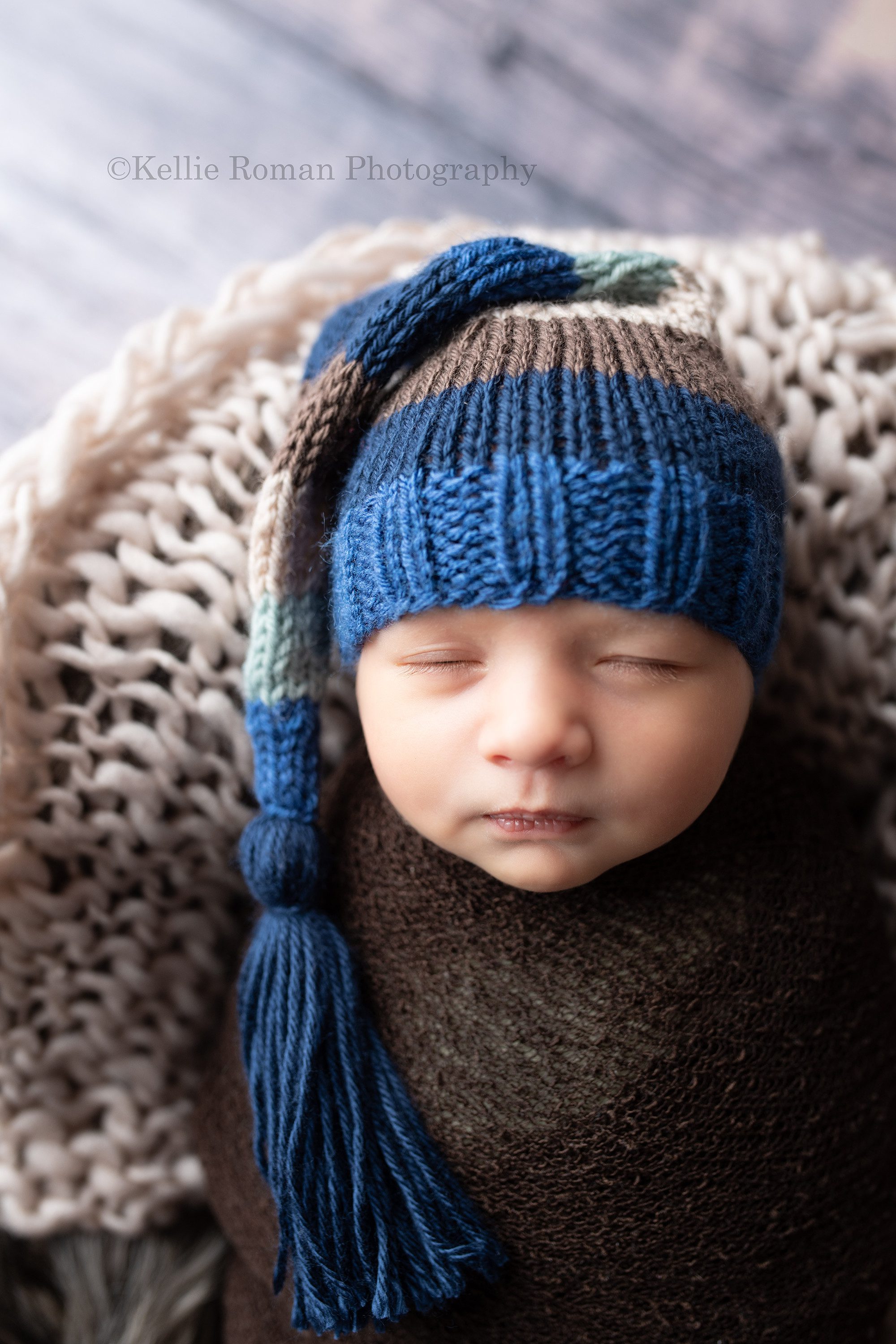 studio newborn session a baby boy is sleeping in a milwaukee photographer studio he is swaddled in a brown fabric while laying in a crate with tan and brown blankets and wraps. He's wearing a striped knit hat with shades of blue ran and brown