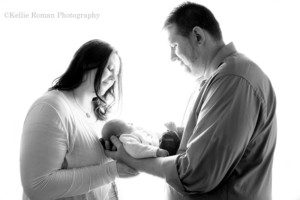 milwaukee newborn a mother and father are holding their infant baby boy in between them, there is very bright backlighting behind them. the image is in black and white