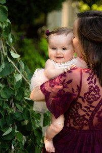 milwaukee family photographer. a close up shot of a mother wearing a long maroon dress holding her baby girl and kissing the side of her daughters head