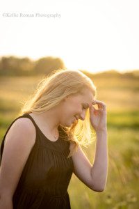senior locations in Milwaukee a senior girl from oak creek is surrounded by sunlight and tall grass she has a black shirt on with jeans and has her hands running through her hair she is looking down and smiling