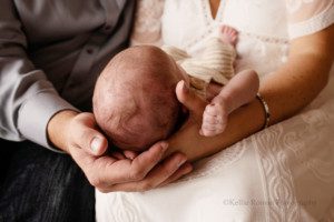 sweet and simple newborn. the image is a close up shot of a mother and father with their hands under the newborn son's head. it's a close up shot of the hands, and the top of the babies head.