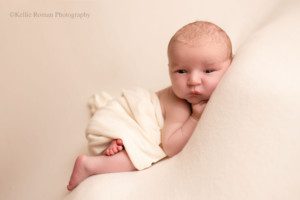 sweet and simple newborn. a baby boy is sleeping on his belly on top of ivory fabric with an ivory swaddle covering his diaper. he's awake and you can see his eyes. he's in a milwaukee photo studio.