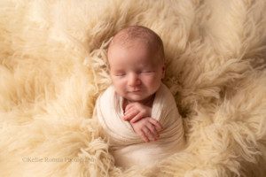 sweet and simple newborn. a baby boy is in a milwaukee photo studio. he is swaddled in an ivory wrap with his hands sticking out. he's snuggled into ivory fur, and he's smiling.