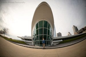 modern milwaukee senior. a milwaukee senior guy from greendale is in downtown milwaukee by the art museum. He's in front of the front of the museum. he's wearing a blue sweater with khakis. the shot is taken with a fisheye lens so it's very wide and the whole sky and museum is in the shot.