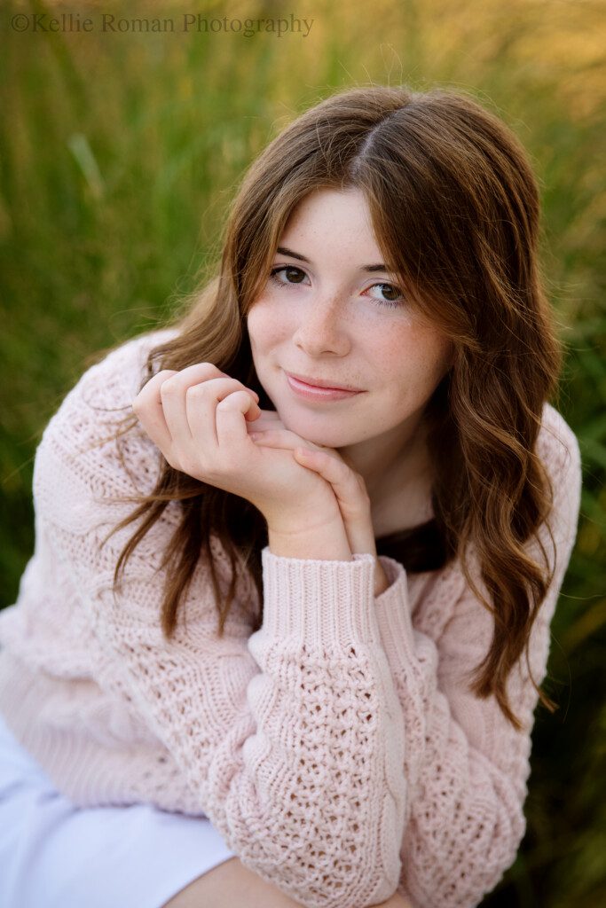 milwaukee senior photography. high school senior girl in milwaukee park. she's sitting with her legs crossed and her chin resting in her hands. elbows are on her knees. she has a pink sweater on, and long brown hair.