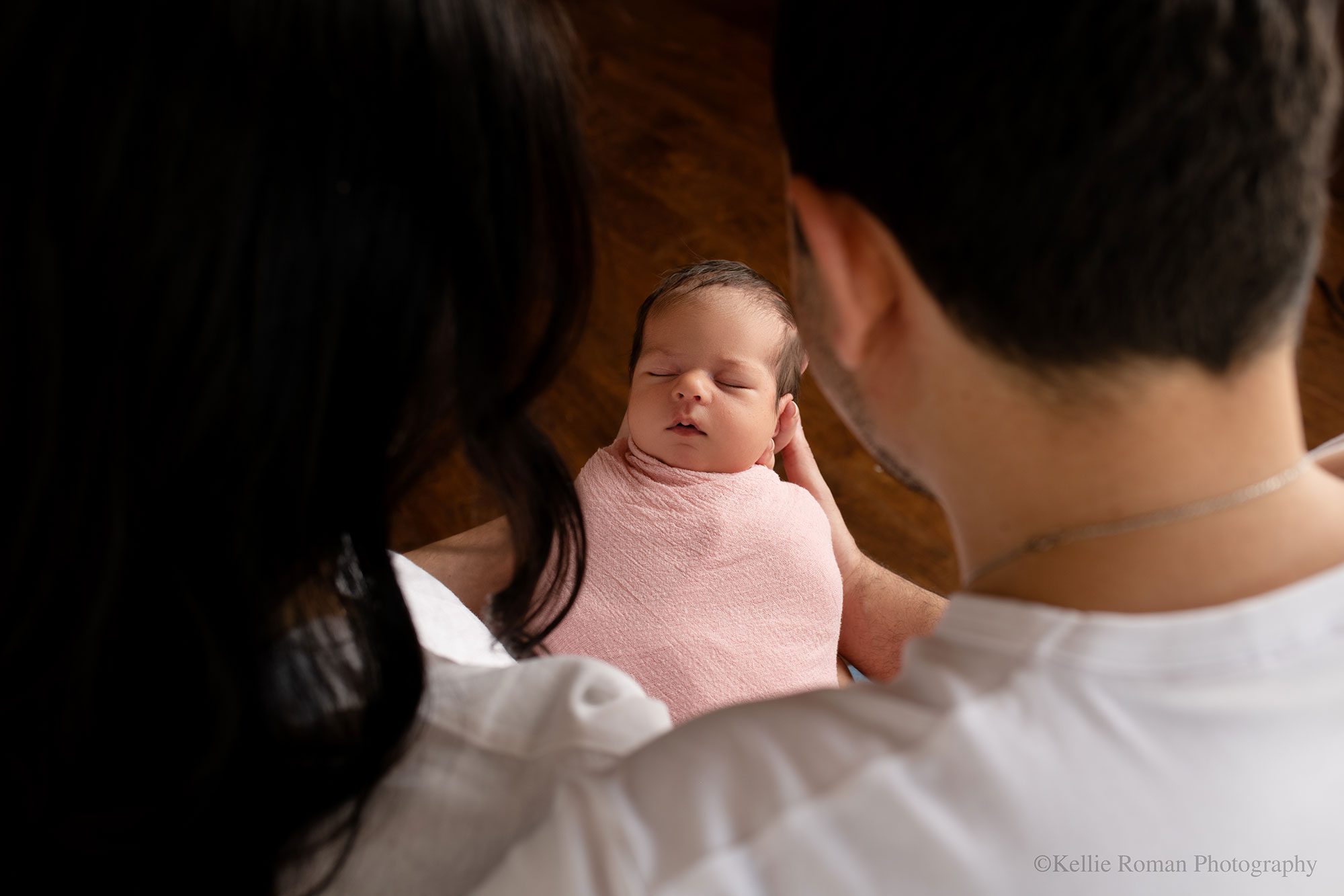 stunning newborn session. the back of the heads of women and man. you see through their heads and they are holding their newborn daughter who's in a pink swaddle wrap. 
