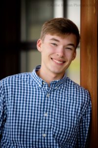 milwaukee senior photographer. close up head shot of Greendale High School senior boy. he's smiling at the camera and has a navy and white checked shirt on.