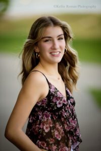 high school senior photographers. close up headshot of senior girl wearing a purple and black flower tank top. she's smiling at the camera while the breeze blows through her long hair.
