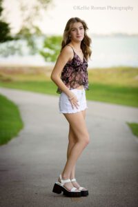high school senior photographers. senior girl standing in a roadway with shorts on a floral tank top on. she's looking at the camera while the breeze blows through her long hair.